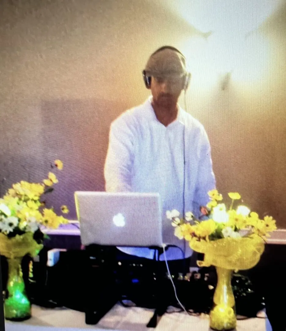 A man in white shirt and headphones standing at table with flowers.