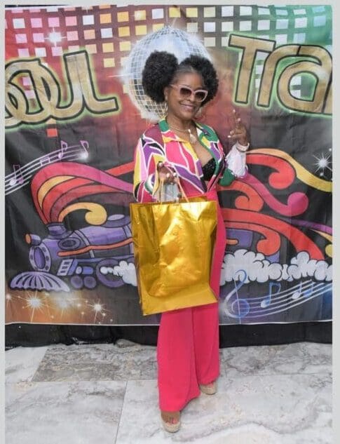 A woman in a colorful outfit holding a gold bag.