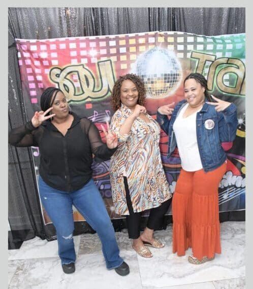 Three women posing for a picture in front of a soul disco banner.