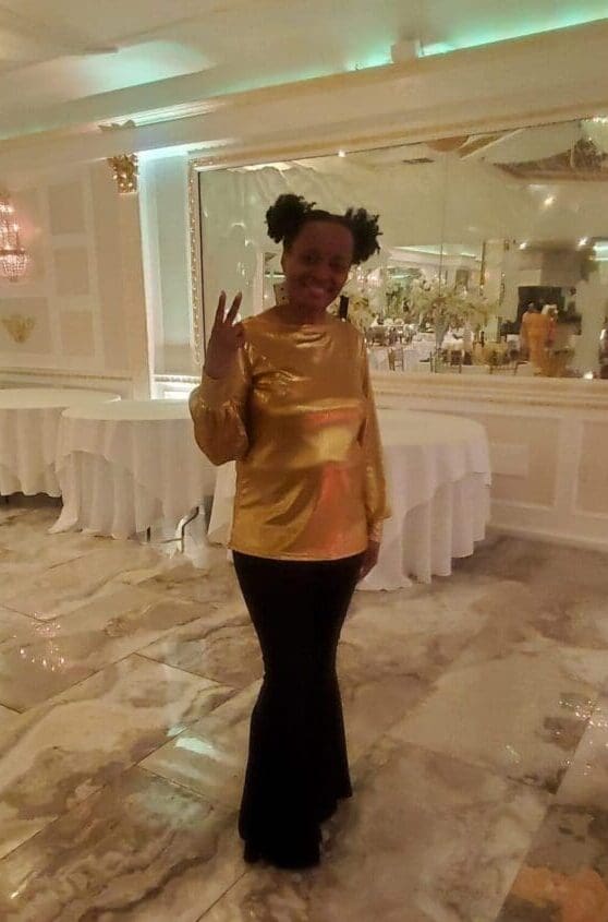 A woman in gold shirt and black pants standing on the floor.