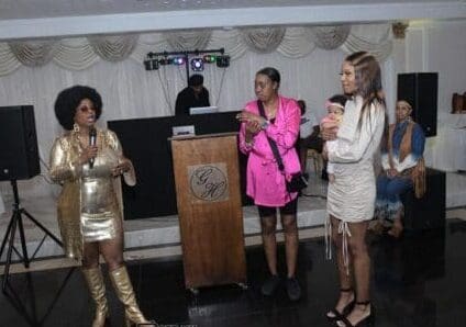 Three women in gold and white outfits standing at a podium.