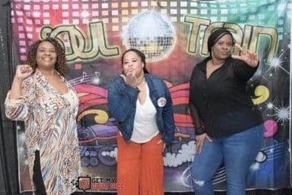 Three women posing for a picture in front of a disco ball.