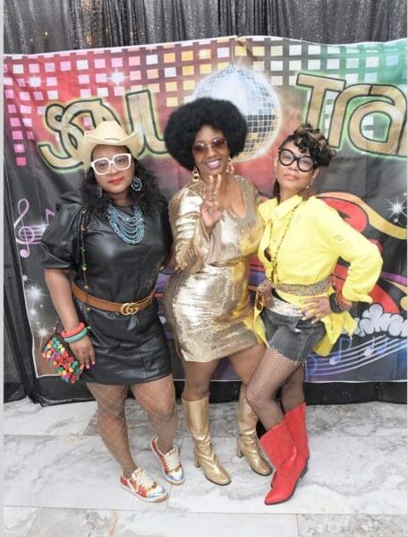 Three women posing for a picture in front of a sign.