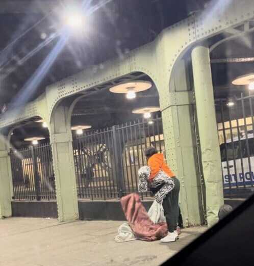 A person sitting on the ground in front of a building.