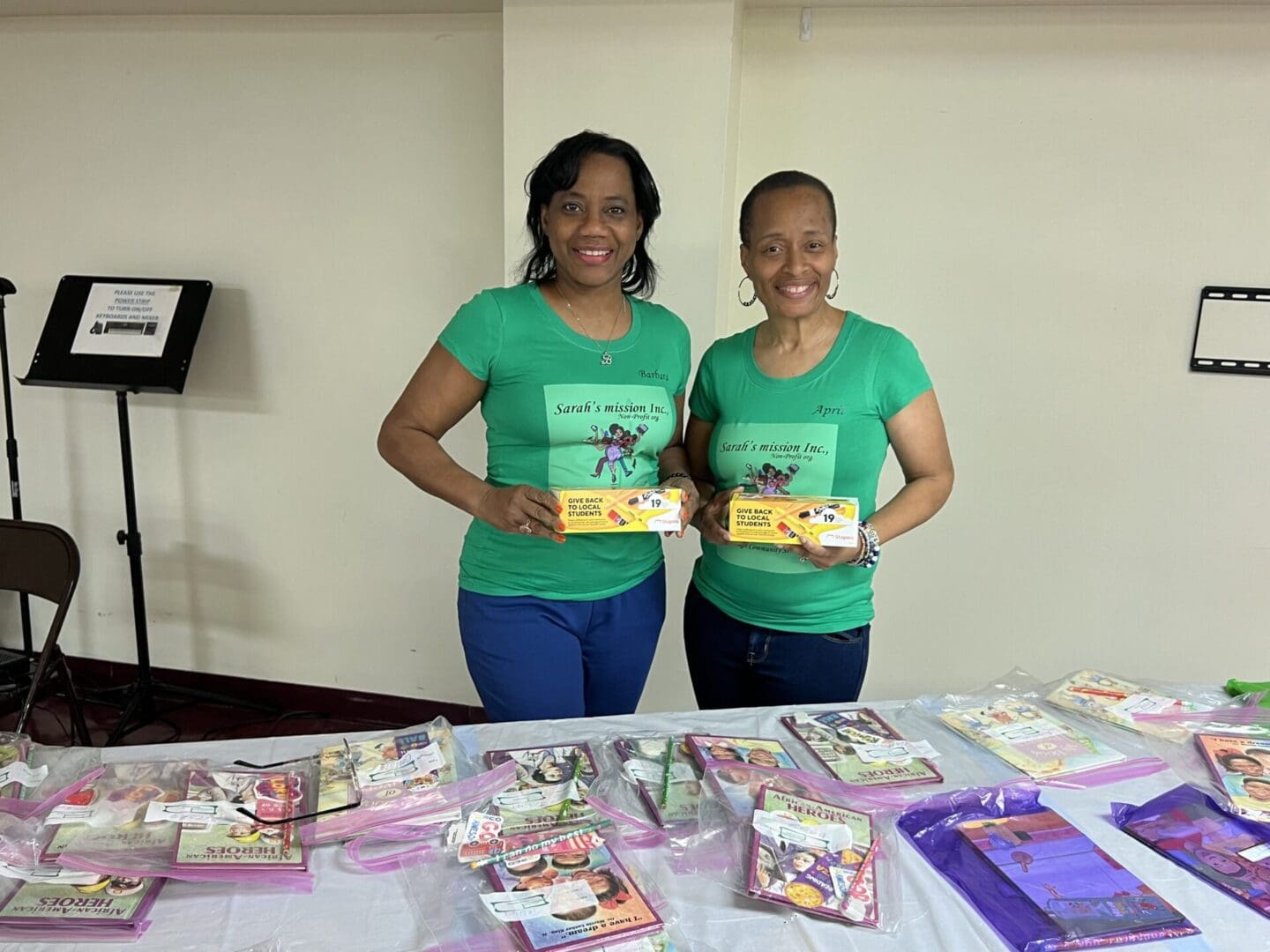 Two women holding up books at a table.