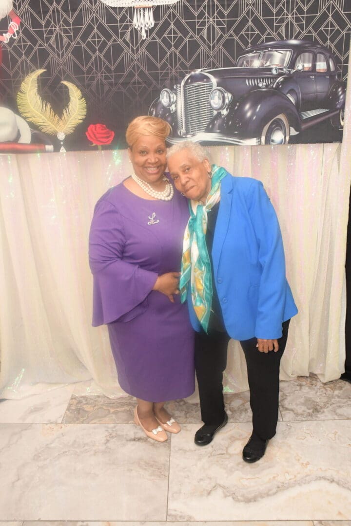 Two women standing next to each other in front of a car.