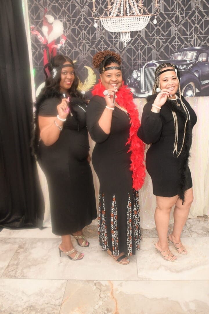 Three women in black dresses and a red head wrap