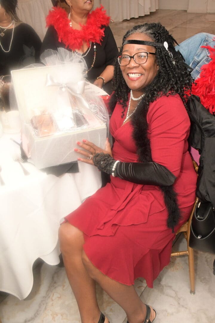 A woman in red dress sitting on chair holding a box.