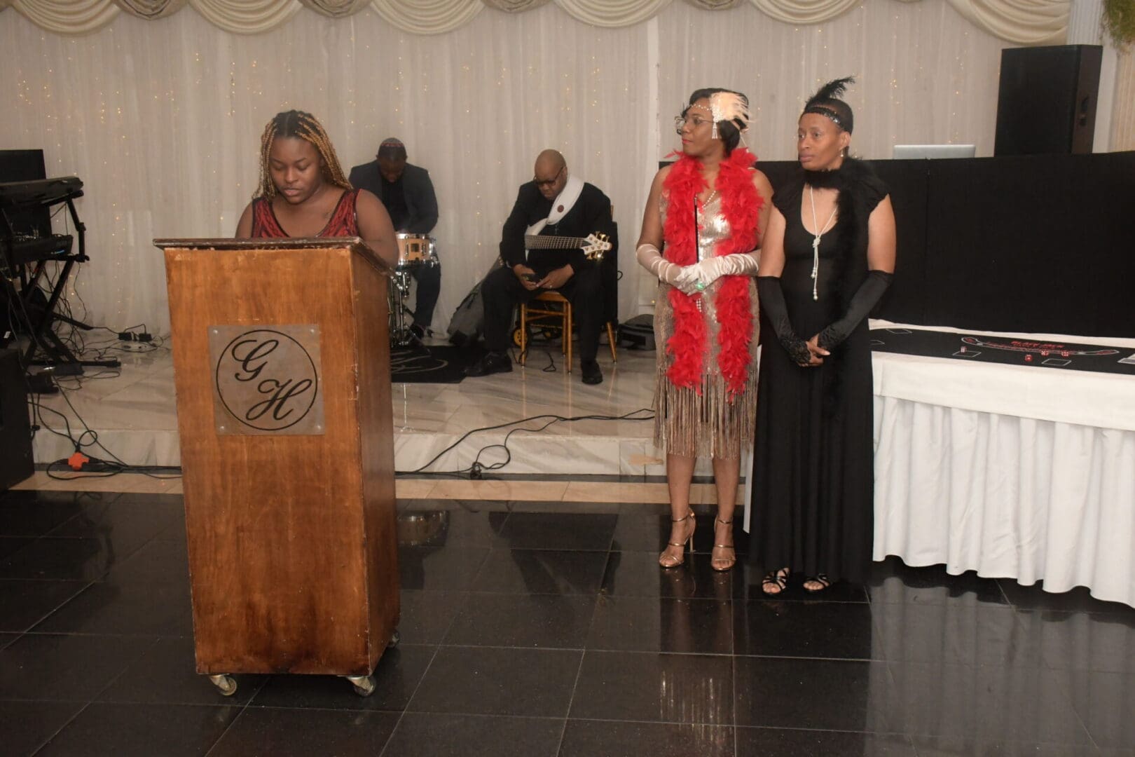 Three women in black and red dresses stand at a podium.