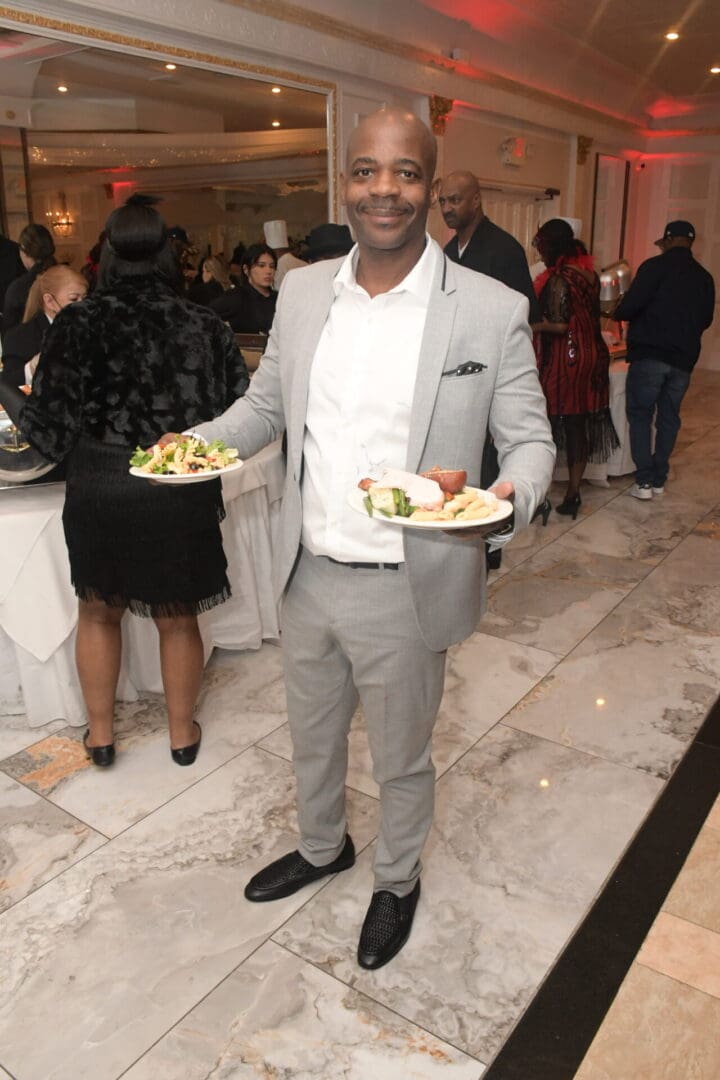 A man in grey suit holding plates of food.