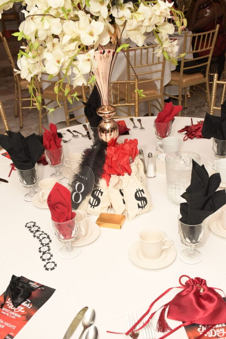 A table set with black and red napkins, white plates and gold cups.