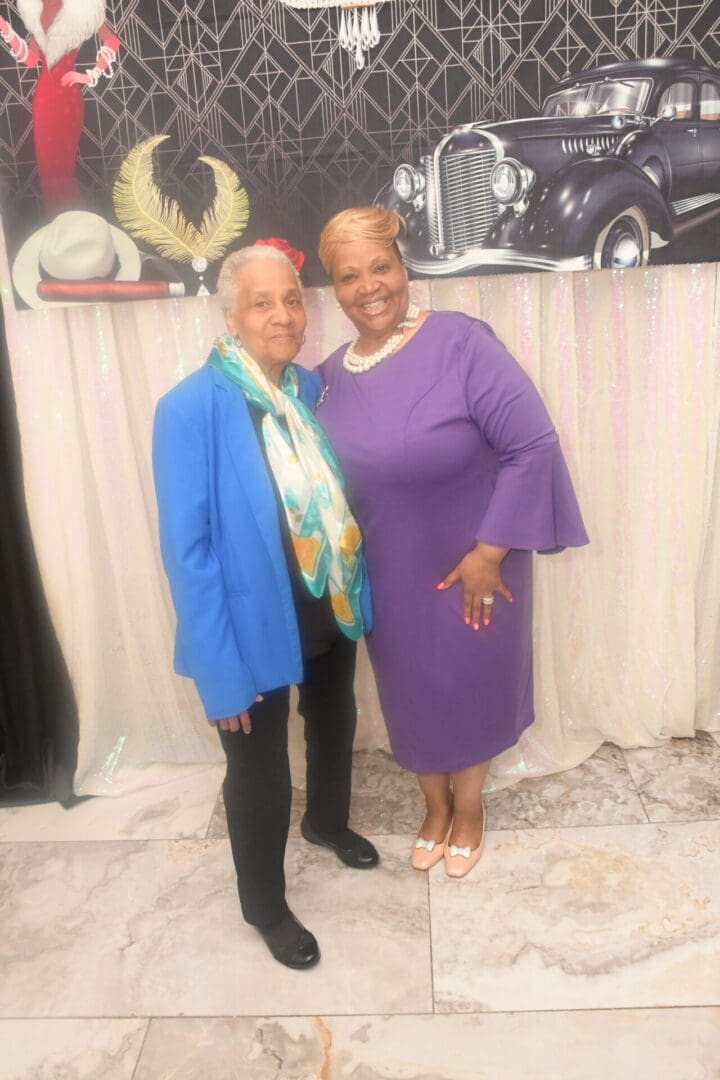 Two women standing next to each other in front of a wall.