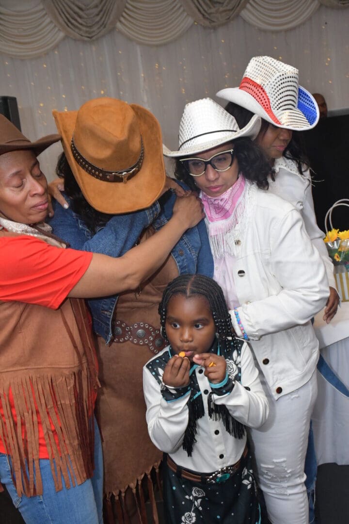 Group in cowboy hats hugging, little girl.