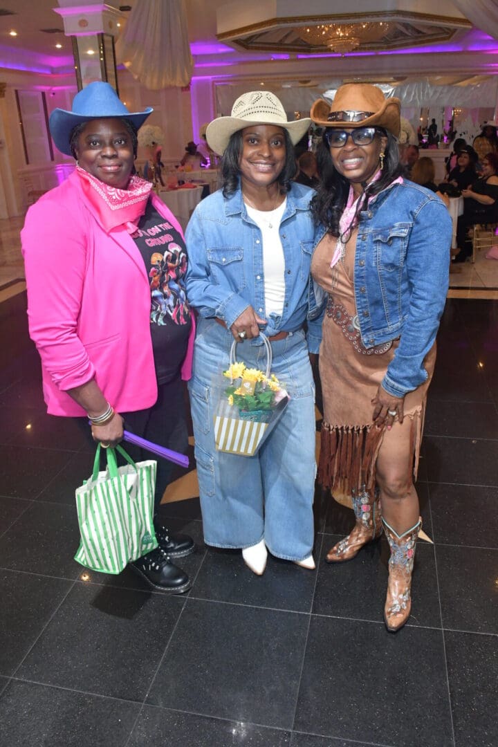 Three women in cowboy hats smiling indoors.