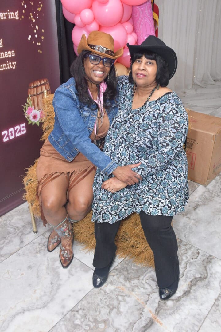 Women in cowboy hats sitting on hay.