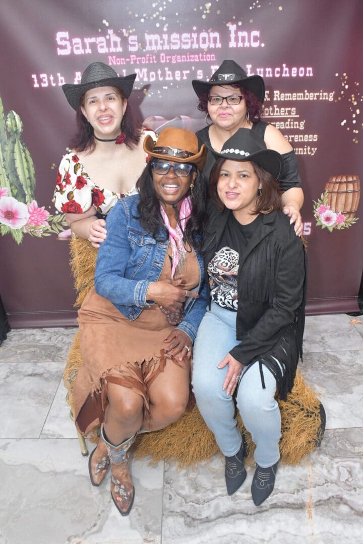 Four women in cowboy hats smiling together.