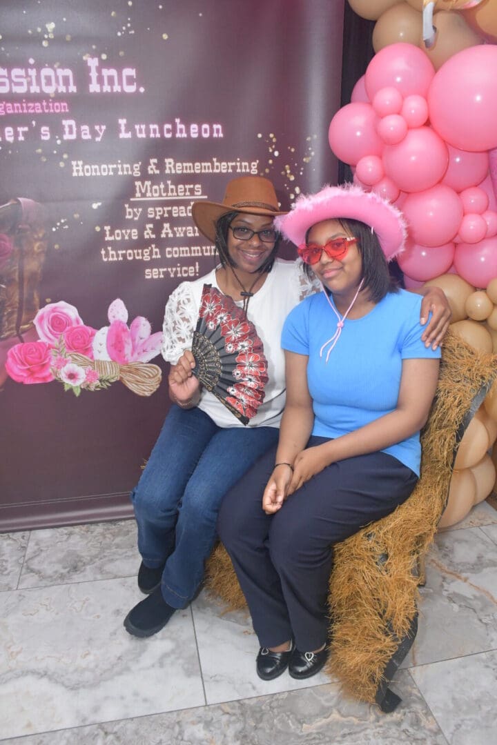 Two women smiling with pink balloons backdrop.